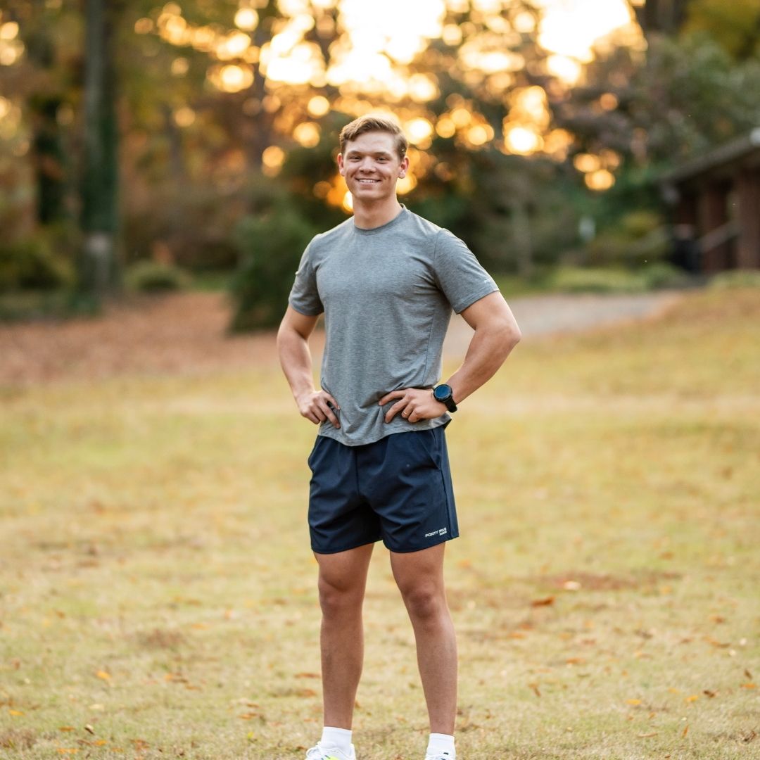 Man in athletic wear standing in a park with trees and sunset in the background