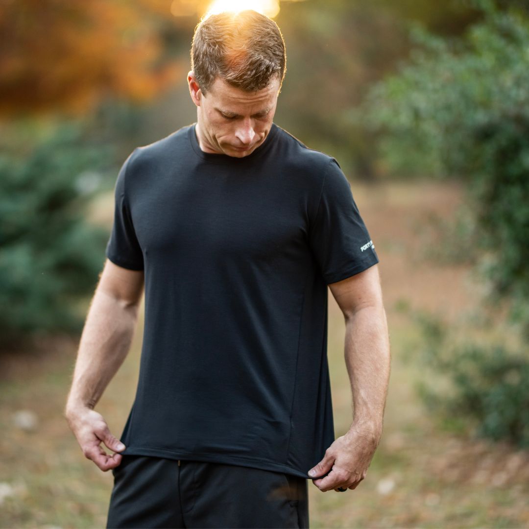 Man wearing a black t-shirt and shorts outdoors with trees in the background