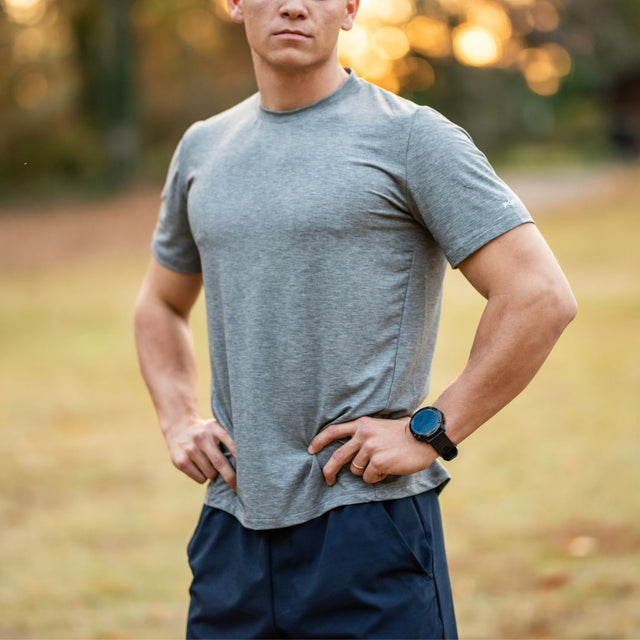 Man wearing a gray t-shirt and navy shorts with a blurred natural background