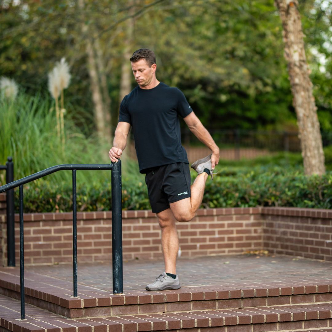 Man stretching outdoors on a brick pathway with greenery in the background