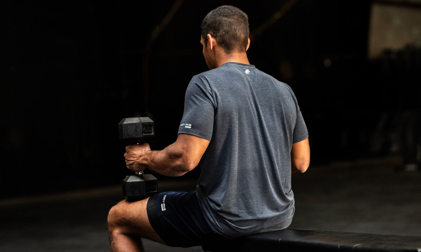 Man sitting on a bench holding dumbbells in a dark setting