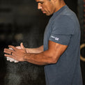 Man in a gym wearing a blue t-shirt with 'Forty Five' logo, applying powder to his hands.