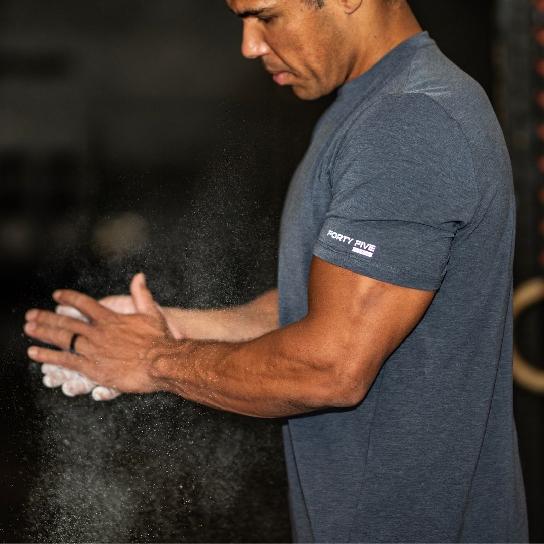 Man in a gym wearing a blue t-shirt with 'Forty Five' logo, applying powder to his hands.