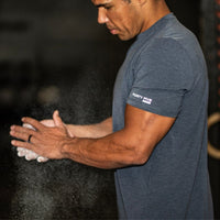 Man in a gym wearing a blue t-shirt with 'Forty Five' logo, applying powder to his hands.