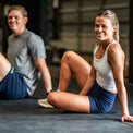 Woman sitting on a mat in a gym with a man in the background