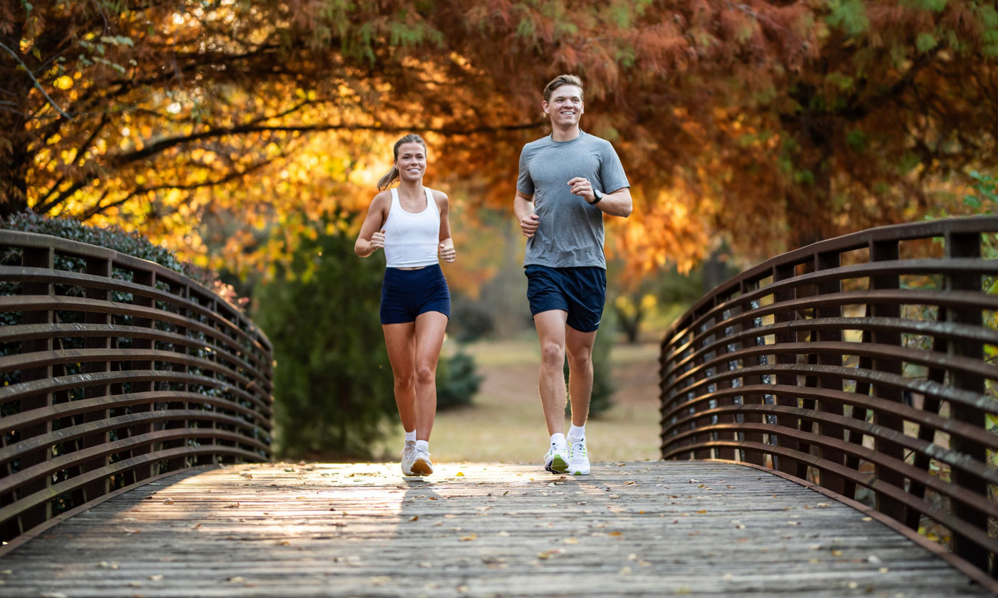 Two people running on a wooden bridge in a park with autumn foliage.