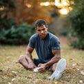 Man sitting on grass tying his shoe outdoors with a blurred natural background