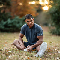 Man sitting on grass tying his shoe outdoors with a blurred natural background