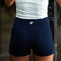 Person wearing navy athletic shorts with a logo on a blurred background